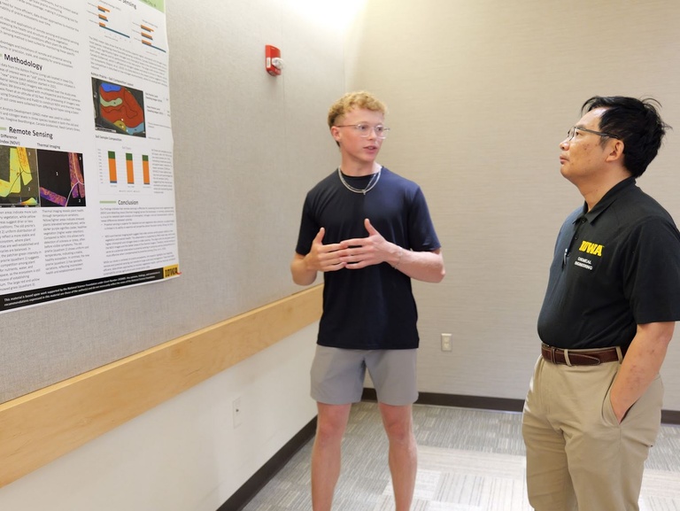 A student discusses his research poster with Jun Wang